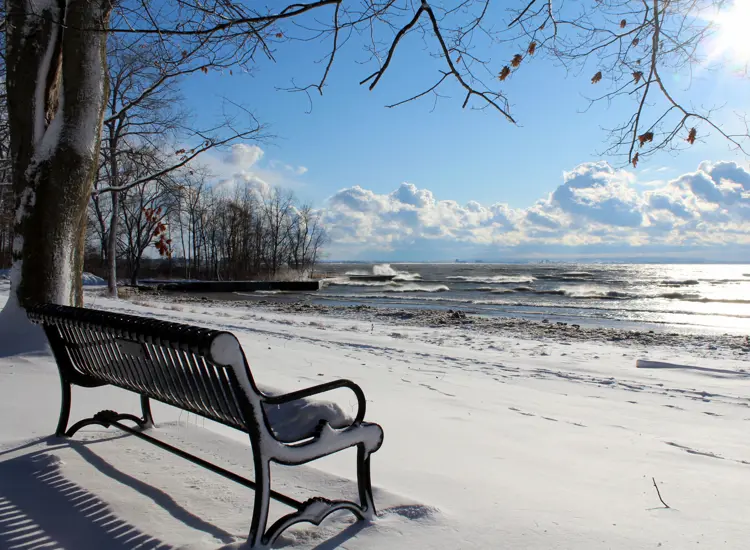 A bench on a path in front of a a snow covered beach